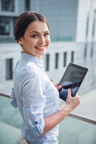 美丽的年轻商业女士是抱着一台平板电脑 看着相机和微笑 站在阳台外的办公大楼 — 图库照片