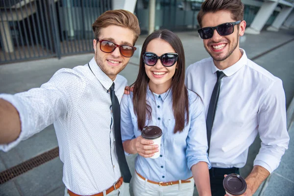 つのハンサムな若いビジネスマン サングラスの女性がコーヒーのカップを持って カメラ目線し笑顔 屋外で立って — ストック写真