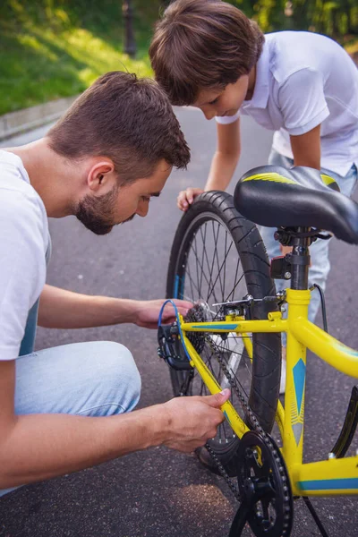 stock image Handsome young dad and his cute little son are riding bikes in park. Father is examining his son's bicycle