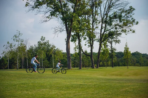 若いお父さんと公園にバイクに乗ってのカジュアルな服で彼の幼い息子のパノラマ ビュー — ストック写真