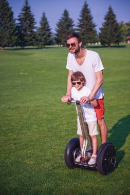 Sevimli küçük çocuk ve yakışıklı babası rahat kıyafetler ve güneş gözlüğü parkta bir segway sürme sırasında gülüyorsun