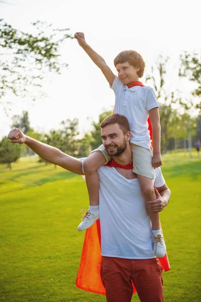 英俊的年轻爸爸和他可爱的小儿子穿得像超级英雄是微笑和拳头的手紧跟在公园里玩耍 — 图库照片