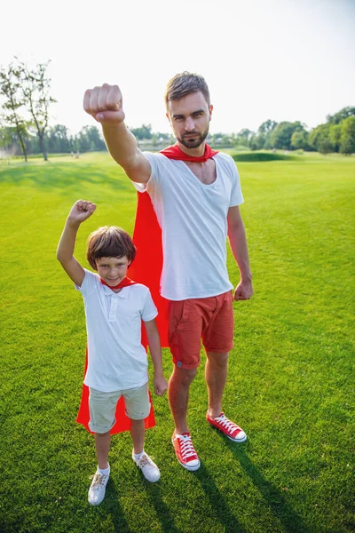 全长肖像的英俊的年轻爸爸和他可爱的小儿子穿得像超级英雄 看着相机和手中的拳头紧跟在公园里玩耍 — 图库照片