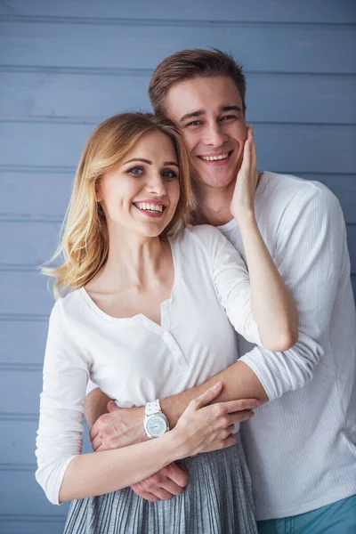 カジュアルな服を着た美しい若いカップルの肖像画は カメラを見て 灰色の壁に立って 笑顔を見て 抱きしめる — ストック写真