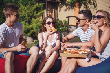 Pizza, iletişim ve gülümseyen, açık havada dinlenme süre fasulye çanta sandalyelere oturan rahat kıyafetler ve güneş gözlüğü güzel gençlerin yemek