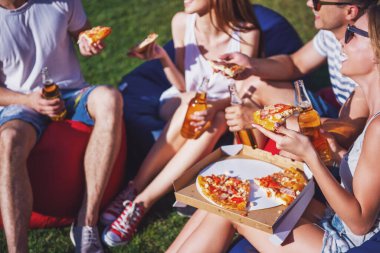 Genç güzel insanlar rahat kıyafetler ve pizza yemek, söz ve gülümseyen, açık havada dinlenme süre fasulye çanta sandalyelere oturan güneş gözlüğü Resim kırpılmış
