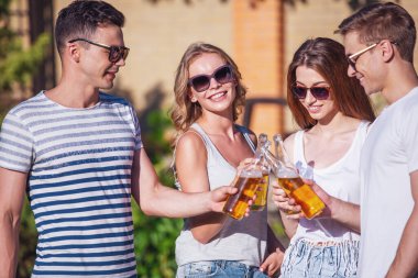 Genç güzel rahat kıyafetler ve güneş gözlüğü tungur şişe içecek ve açık havada dinlenme süre gülümseyen insanlar. Bir kız kameraya bakıyor