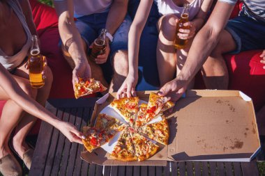 Pizza yeme ve içme, açık havada dinlenme süre fasulye çanta sandalyelere oturan rahat kıyafetler içinde güzel gençlerin Resim kırpılmış