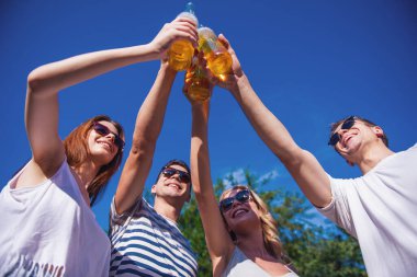 Düşük açılı görünüş güneş güzel gençlerin tungur şişe içecek ve açık havada dinlenme süre gülümseyen gözlük