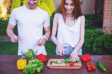 Yakışıklı kesme sebze salatası, kızla konuşmak ve açık havada yemek yaparken gülümseyen biri