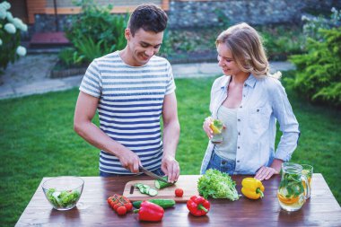 Yakışıklı kesme sebze salatası, kızla konuşmak ve açık havada yemek yaparken gülümseyen biri