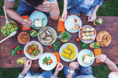 Güzel gençlerin kırpılmış oturma sırasında tablo ve sahip piknik açık havada, lezzetli yemek yeme Üstten Görünüm