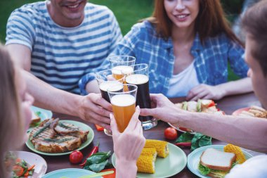 Gençlerin bardakları tokuşturup ve masada oturan ve açık havada piknik gülümseyen güzel Resim kırpılmış