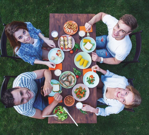 stock image Top view of young beautiful people eating delicious food, looking at camera and smiling while sitting at the table and having picnic outdoors