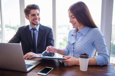 Güzel genç iş kadını ve yakışıklı işadamı resmi elbiseli bir dizüstü bilgisayar kullanarak, belgeleri tartışırken ve ofiste çalışırken gülümseyen