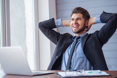 Eller başının arkasına tutmak, ofiste çalışırken gülümseyen ve uzağa bakarak resmi kıyafetli yakışıklı genç işadamı portresi