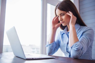 Güzel genç yorgun iş kadını ofiste çalışırken bir laptop kullanıyor