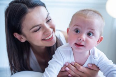 Güzel genç anne ve onun tatlı küçük bebek gülümseyerek, evde yatakta yatarken portre