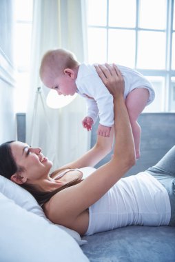 Tatlı küçük bebeği tutarak, gözü üstünde ve evde yatakta yatıyordu süre gülümseyen güzel genç anne yan görünüm