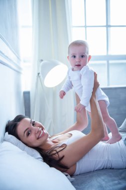 Güzel genç anne onun tatlı küçük bebek evde yatakta yatarken Ise tutarak yan görünüm. Her ikisi de ona bakarak ve gülümseyen