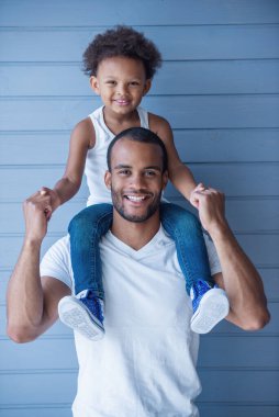 Yakışıklı genç Afro Amerikalı baba ve onun sevimli çocuğunportre kamera bakarak ve gülümseyerek. Çocuk babamın omuzlarında oturuyor.