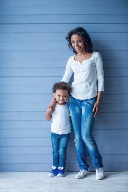 Güzel genç Afro Amerikalı anne ve onun sevimli çocuk tam uzunlukta portre kamera bakarak ve gülümseyerek, gri arka plan üzerinde duran