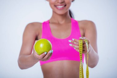 Bir elma ve mezura tutarken gülümseyen güzel bir sporcunun beyaz arka planda izole edilmiş görüntüsü.