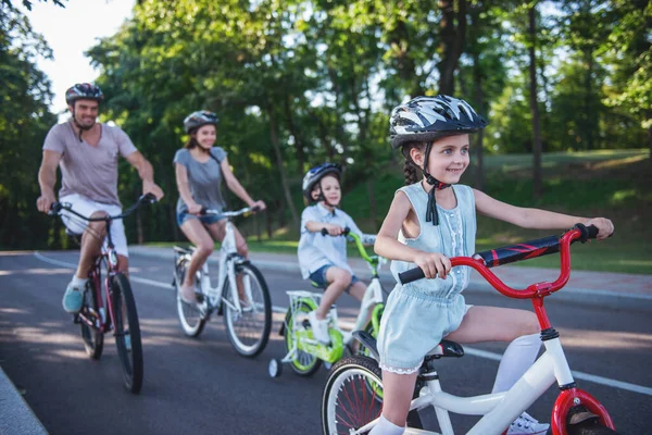 Happy family is riding bikes outdoors and smiling. Little girl in the foreground
