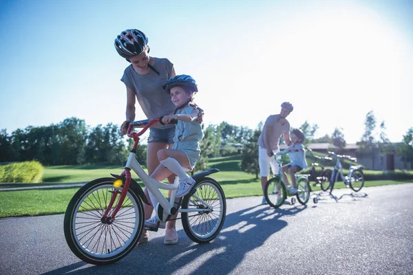 Happy family is riding bikes outdoors and smiling. Parents are teaching their children