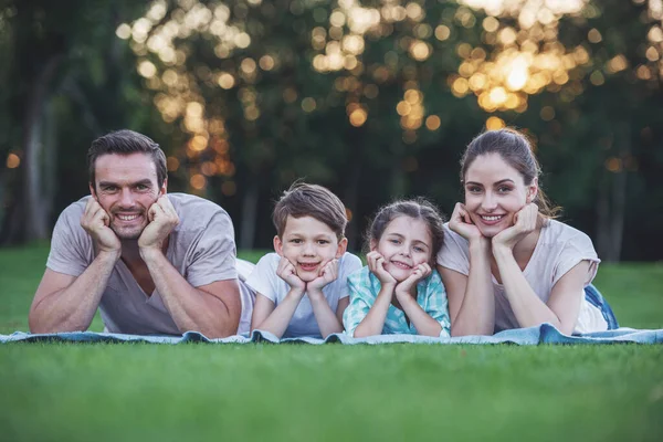 Portrait of beautiful happy family looking at camera and smiling while lying on the grass in the park, leaning in hands