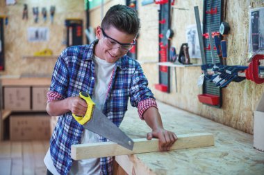 Koruyucu gözlük yakışıklı genç marangoz ahşap ve atölye bir testere ile çalışırken gülümsüyor