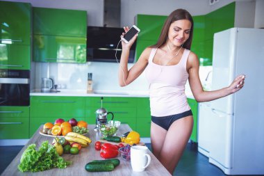 Iç çamaşırı ve kulaklık güzel seksi kız bir akıllı telefon kullanarak müzik dinliyor, dans ve mutfakta yemek yaparken gülümseyerek