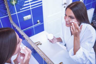 Onun yüzüne dokunmaktan ve banyodaki aynaya bakarken gülümseyen güzel genç kadın portresi