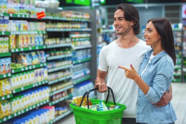 Güzel genç çift konuşmak ve süpermarket gıda seçerken gülümseyerek. Adam bir alışveriş sepeti tutuyor