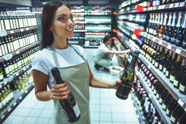 Önlük güzel pazarlamacı süpermarket içecek şişe düzenlenmesi sırasında gülümsüyor