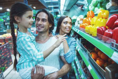 Güzel anne ve sevimli küçük kızları konuşuyor ve süpermarket gıda seçerken gülümseyerek. Kız Baba'nın silah oturuyor