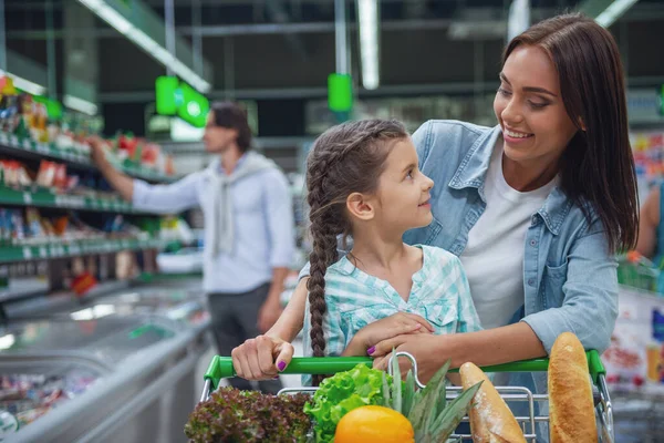 Family in the supermarket. Beautiful young mom and her little daughter are looking at each other and smiling, in the background dad is choosing goods