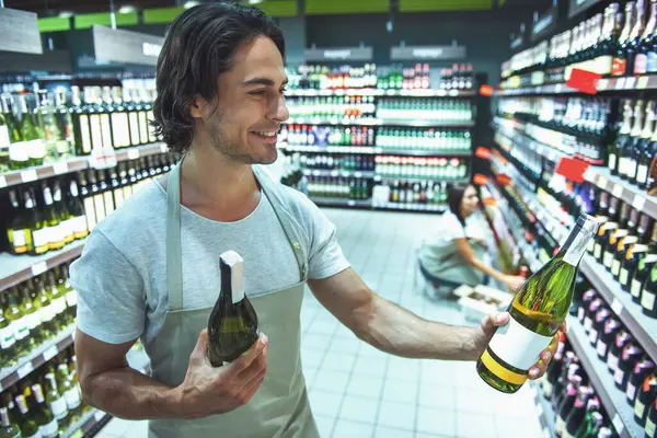 Önlük yakışıklı satıcı süpermarket içecek şişe düzenlenmesi sırasında gülümsüyor