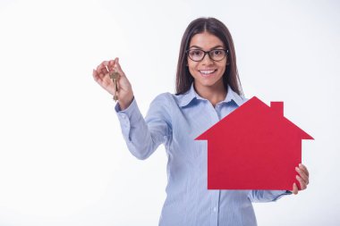 Klasik gömlek ve gözlük güzel genç iş kadını bir kağıt ev ve anahtarları tutuyor, kamera bakıyor ve gülümseyerek, beyaz izole