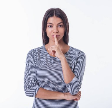 Rahat giysiler içinde güzel genç kız sessizlik işareti gösteriyor, dudaklarında parmak tutmak ve kameraya bakarak, beyaz izole