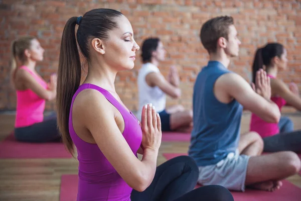 Side view of beautiful sports people sitting in lotus position while doing yoga in modern fitness hall