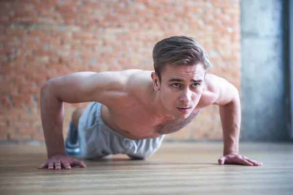 Handsome sportsman is doing push ups while working out in modern fitness hall