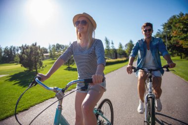 Güzel şık çift parkta Bisiklete binme süre gülümsüyor