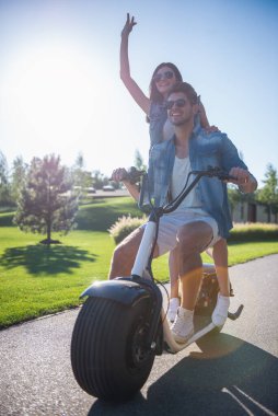 Güzel şık çift parkta elektrikli scooter üzerinde sürme sırasında gülümsüyor