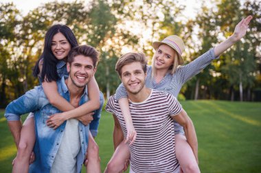 Kameraya bakarak ve parkta istirahat ederken gülümseyen güzel şık arkadaşlar. Kızlar pickaback