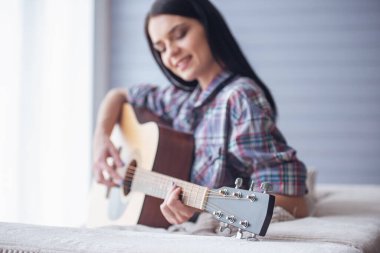 Çekici genç kız gitar çalmak ve evde kanepede otururken gülümseyen