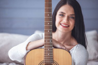Çekici genç kız bir gitar holding, kameraya bakıyor ve yerde evde otururken gülümseyen
