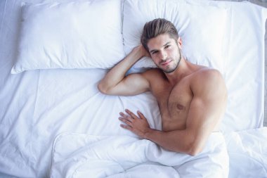 Seksi kas genç adam yatakta yatarken şehvetli gülümseme ile kameraya bakan Üstten Görünüm