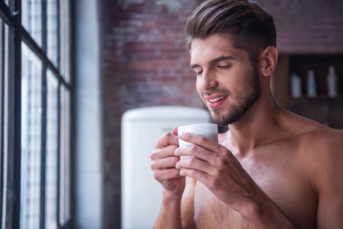 Seksi genç adam çıplak gövde ile bardağı, kokulu ve evde mutfakta dururken gülümseyen götürüyor