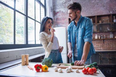 Güzel genç çift birbirine bakarak ve evde mutfakta yemek yaparken gülümseyerek. Kesme sebze adamdır